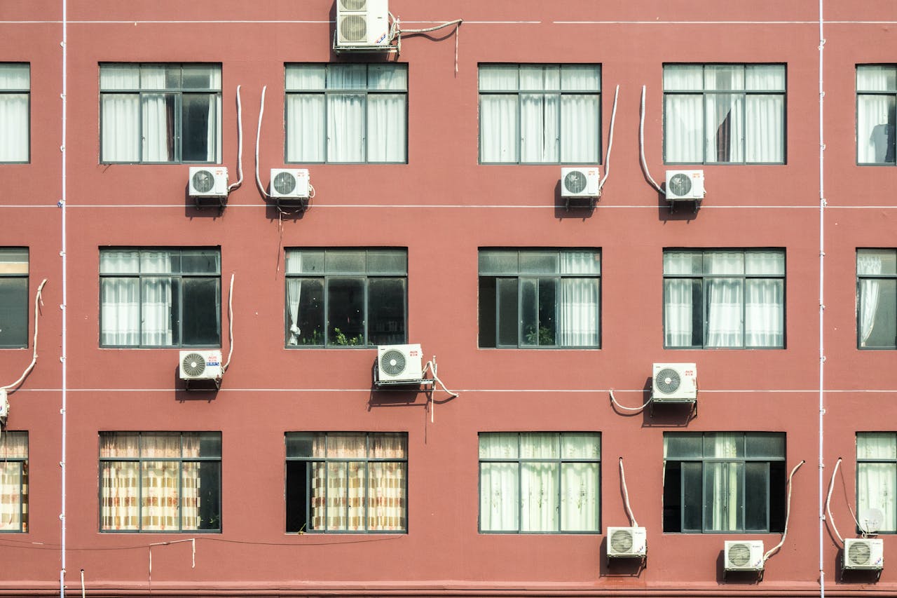 Red building exterior with multiple windows and air conditioners, showcasing urban architecture.